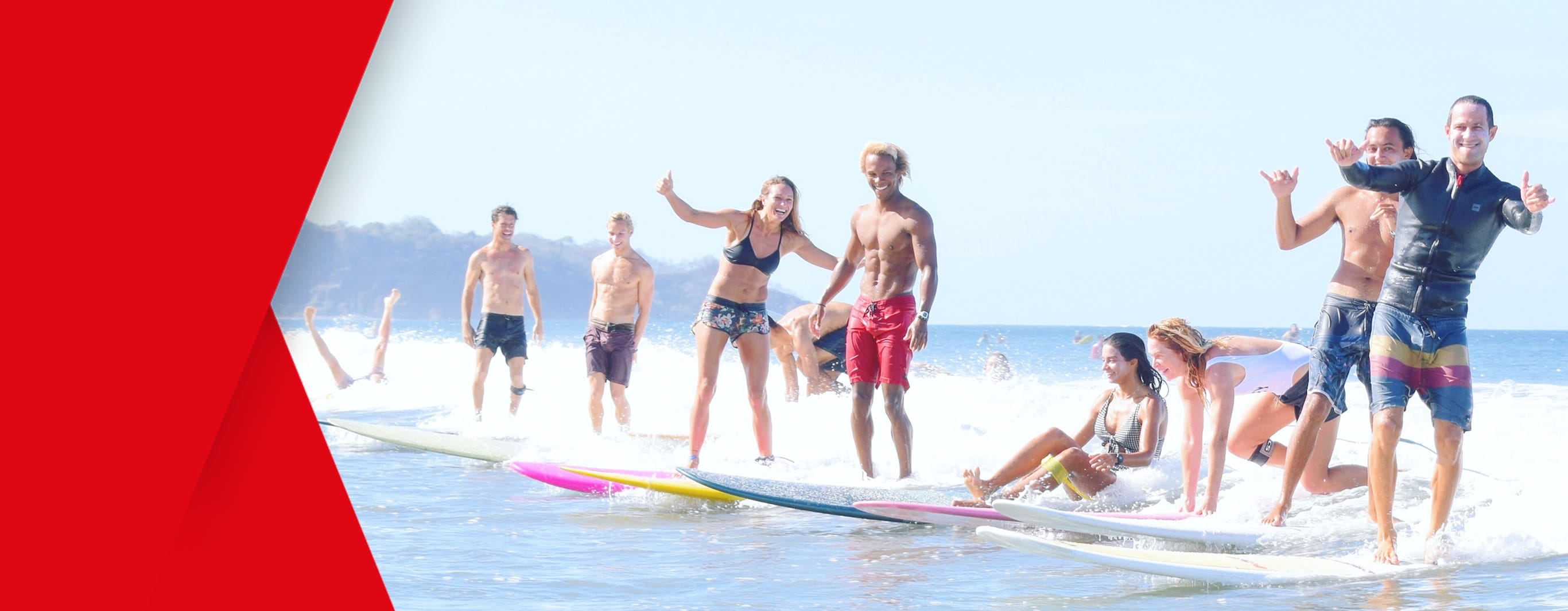 A group of nine surfers smile and wave for the camera as they ride the waves to the shore