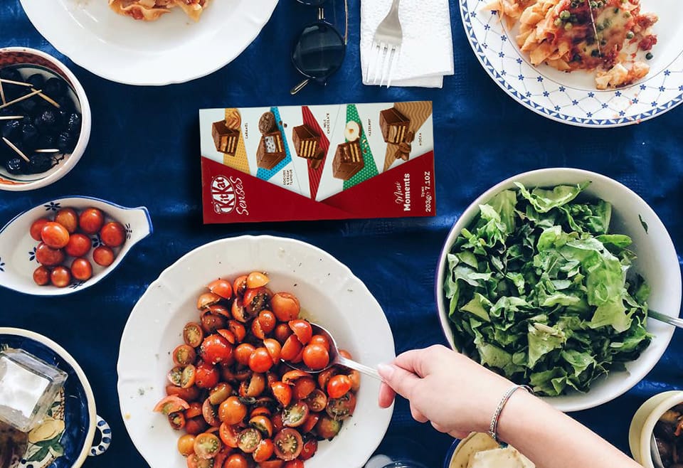 A box of KitKat chocolates is nestled amongst a tabletop of several delicious looking Italian salad dishes
