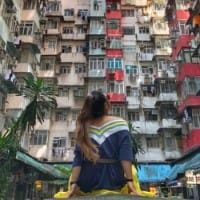 A woman sits in the courtyard of colourful residential apartments and looks towards the unseen sky